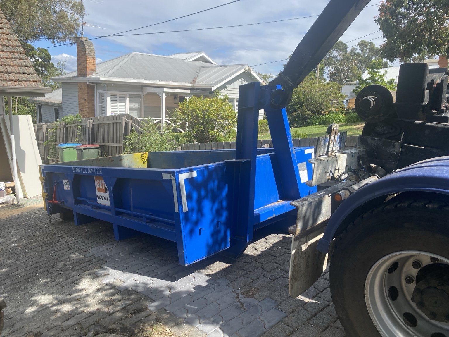 A GetBins hook truck placing a blue bin on a residential driveway.