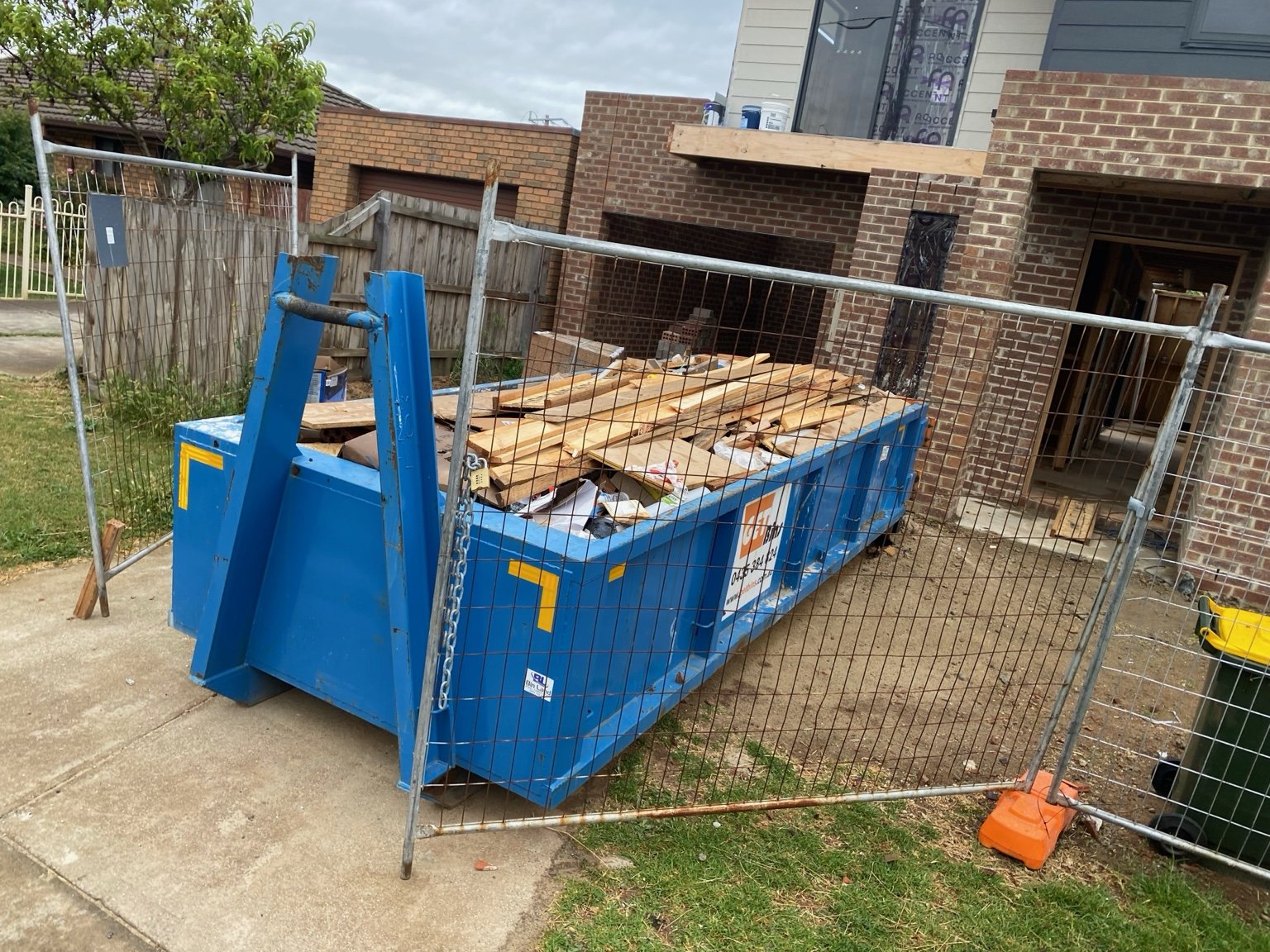 A GetBins blue skip filled with timber and building materials beside a construction site.