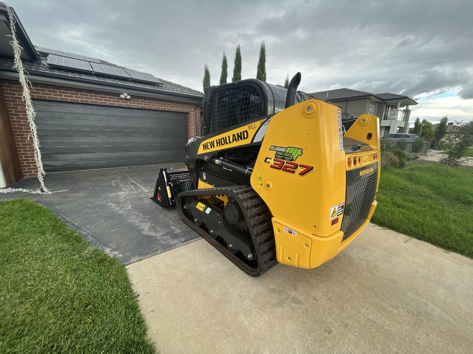 A yellow compact tracked loader beside a residential driveway.