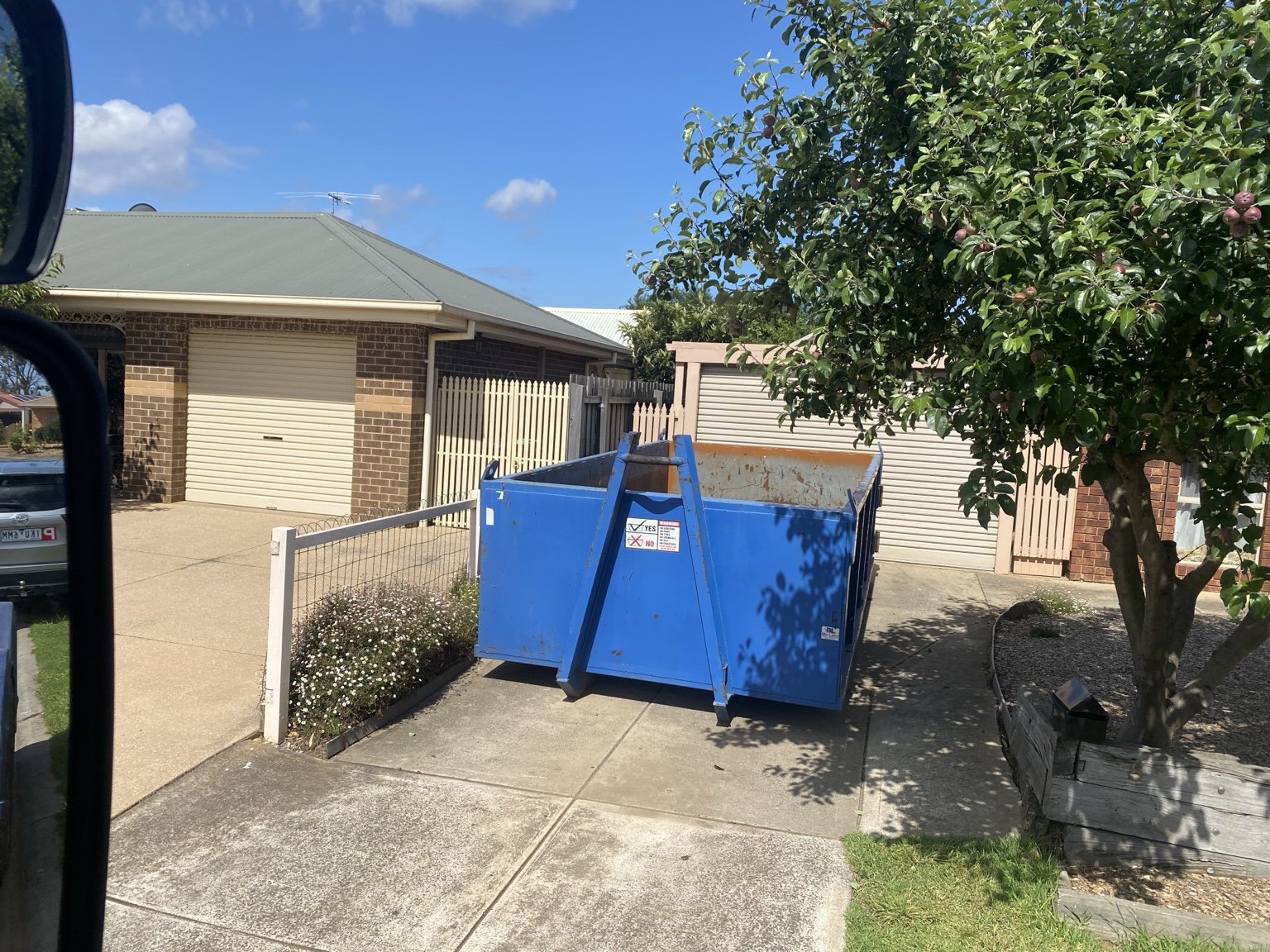 A blue GetBins skip bin placed on a driveway beside a home.