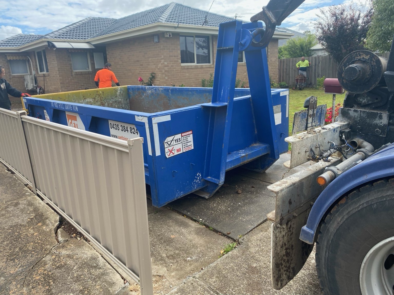 A GetBins bin being lowered into a residential property using a hook truck.