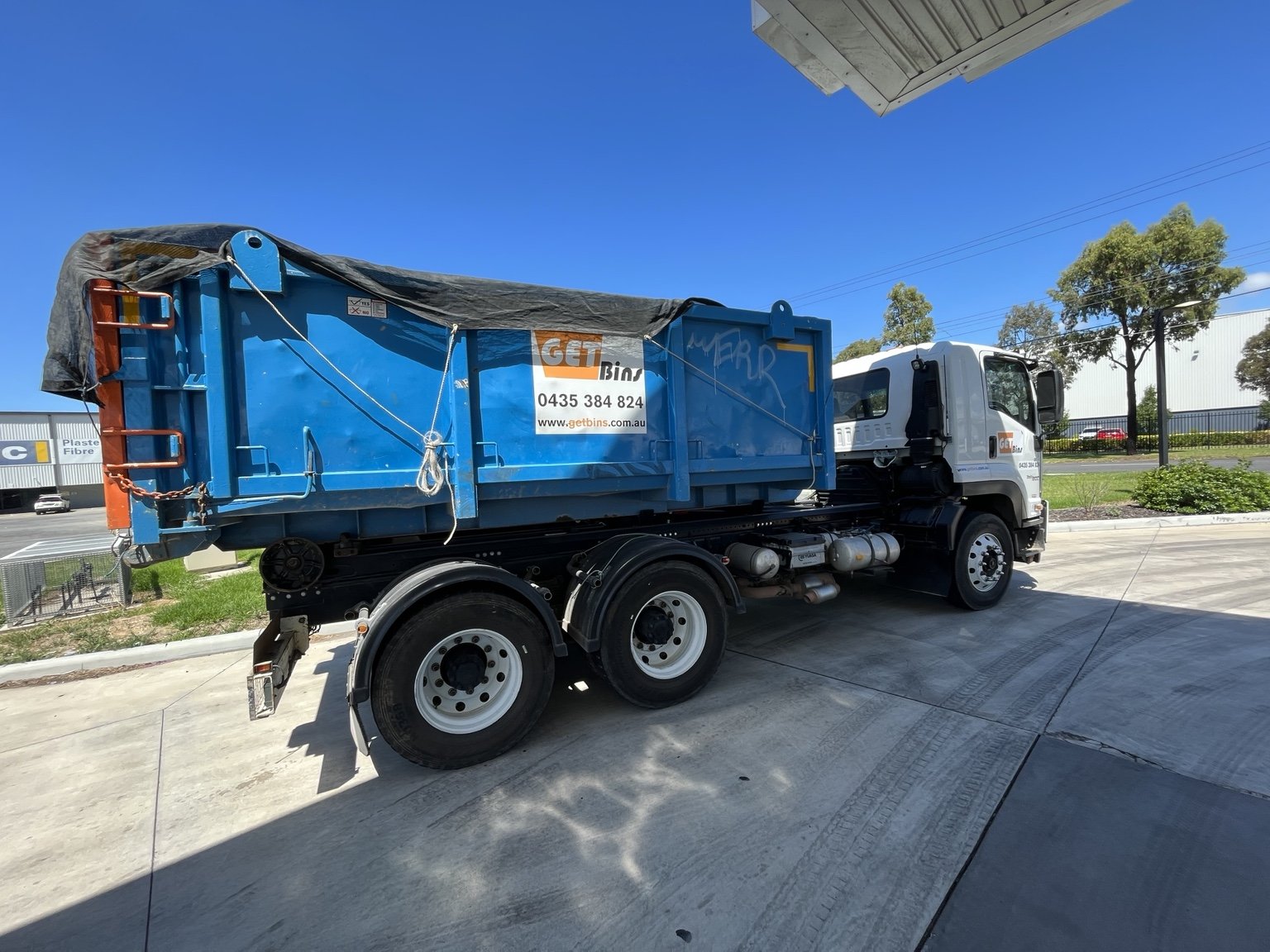 A white GetBins hook truck transporting a large blue waste bin.