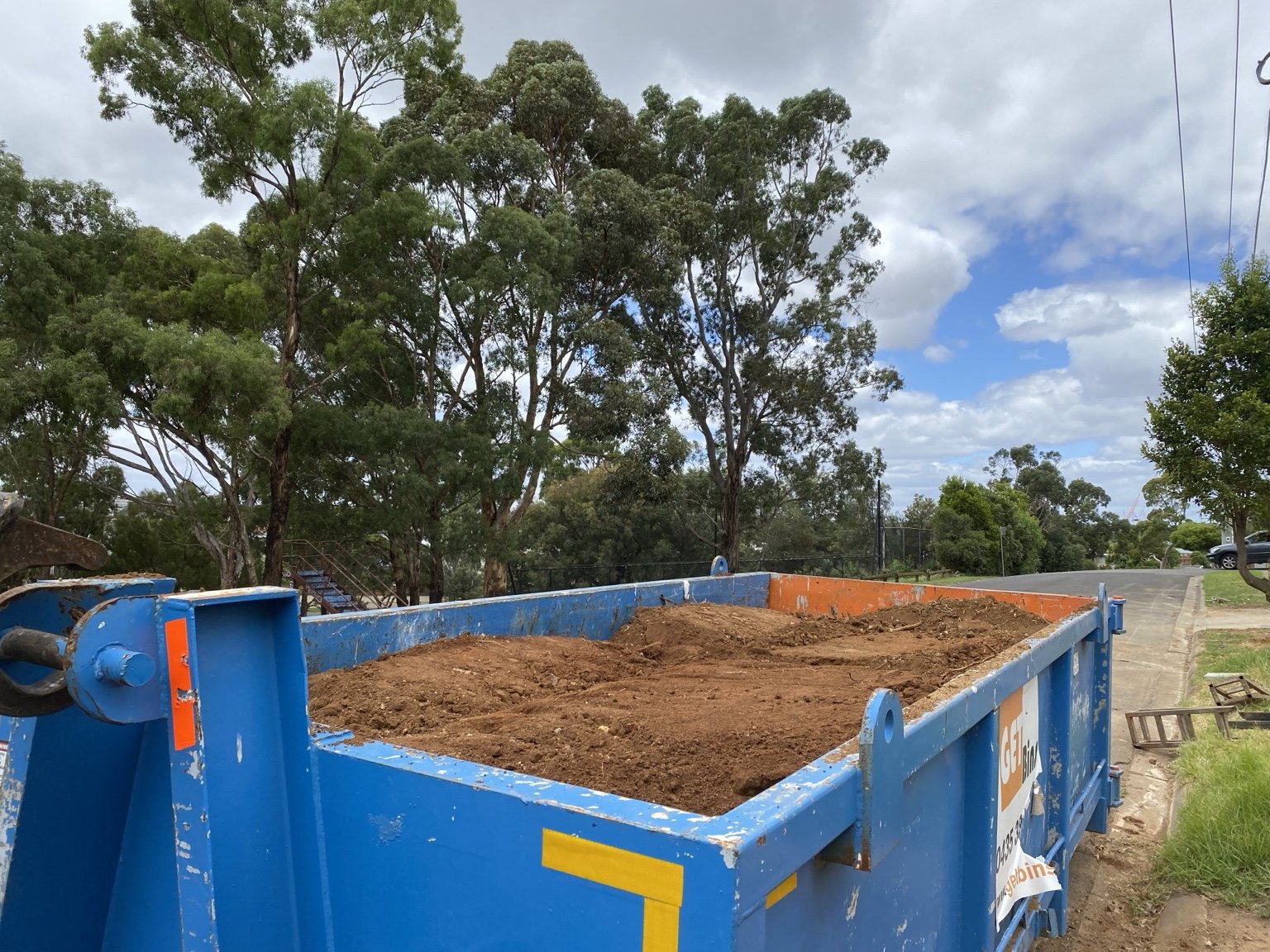 A blue GetBins bin loaded with soil and positioned on site.